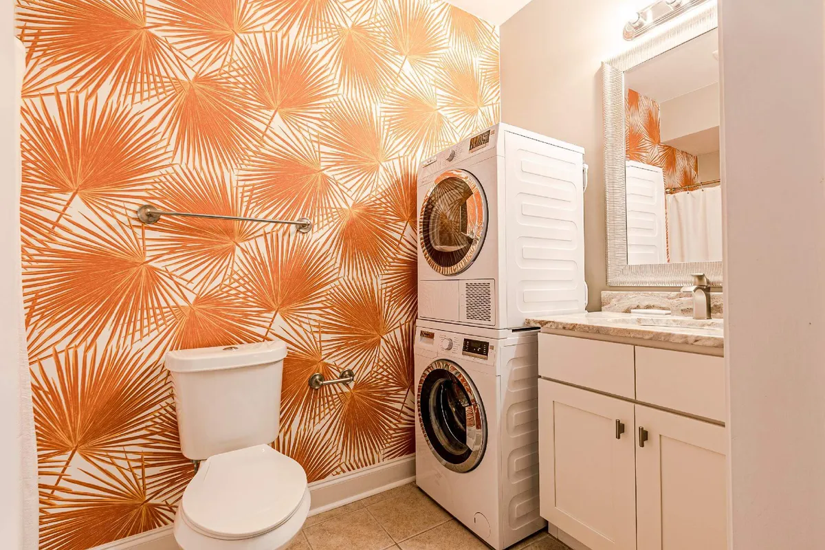 This image centers on a vanity with a mirror, complemented by bold wallpaper and a washer/dryer unit nearby. The vanity area, with its mirror and surface, visually conveys the concepts of counter space, self-care, and grooming—echoing the section’s notes about luxury routines and thoughtful touches.