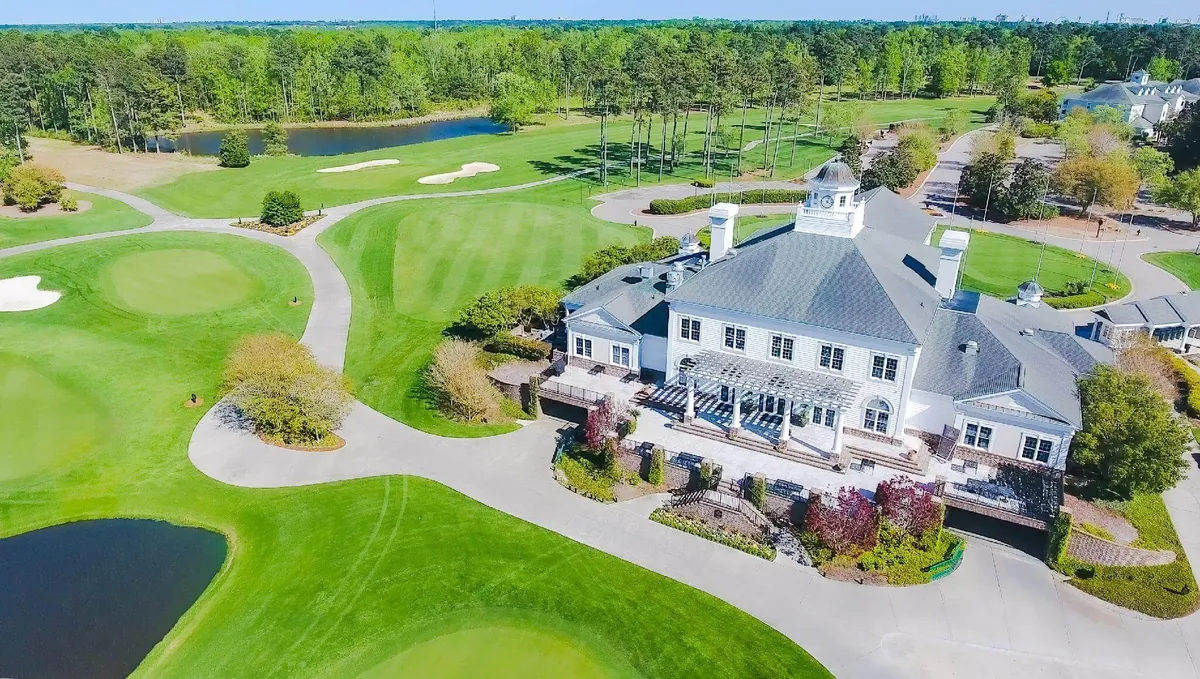 An elegant exterior shot of the clubhouse nestled beside a golf course and water features. The clubhouse provides a sophisticated backdrop for social gatherings and events, set amid serene landscaping and lush greens.