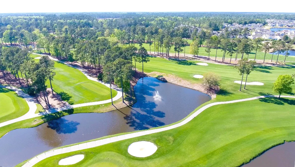 This image captures the lush green fairways and golf greens of a scenic course, accentuated by sparkling water features and framed by tall trees. The scene is serene yet dynamic, giving a sense of the challenge and beauty that await golfers on the course.