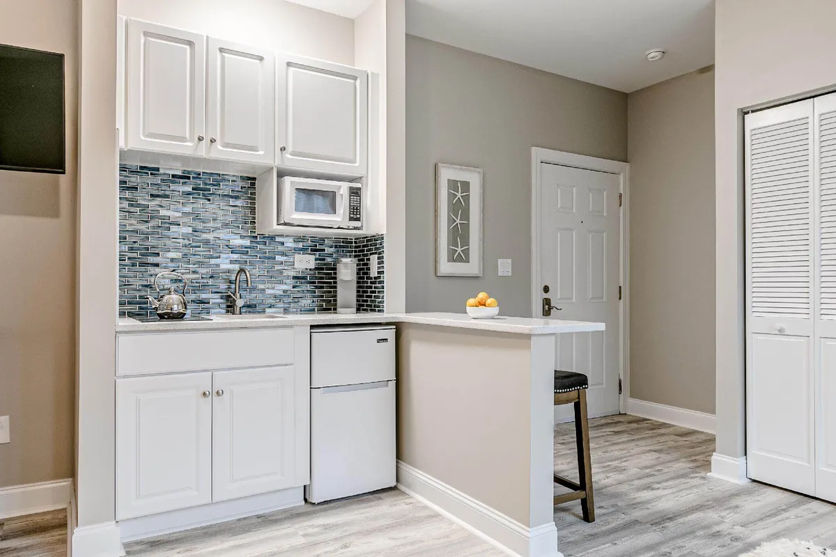 A cozy and modern interior view of a bar area, featuring a kitchenette, bar stool, and a stylish backsplash. The space feels intimate and perfect for casual happy hours or evening cocktails in a resort setting.