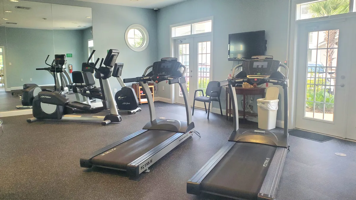 This interior scene shows a modern fitness center, equipped with treadmills, elliptical machines, and large windows that let in plenty of natural light. The mirrors and sleek equipment create a motivational environment for workouts and fitness classes.