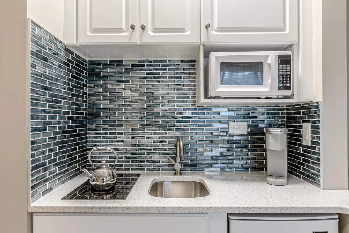 A sleek kitchenette area with a kettle, sink, microwave, and striking backsplash tile. Sunlight streams in, creating a warm and inviting space for meal preparation or enjoying a morning beverage together.